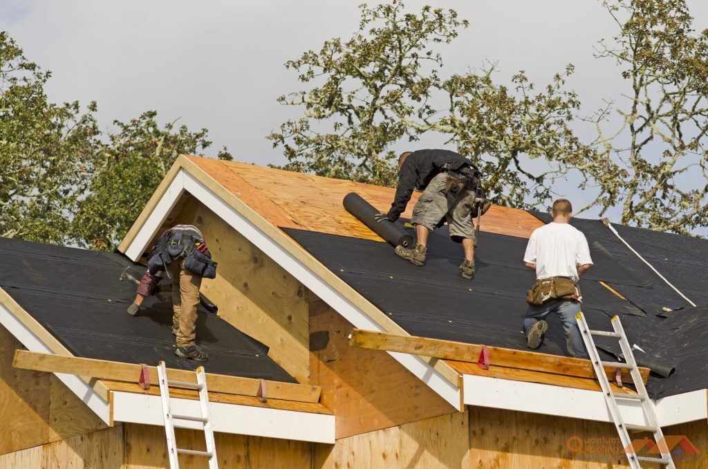Three roofers installing underlayment and decking on a gable roof
