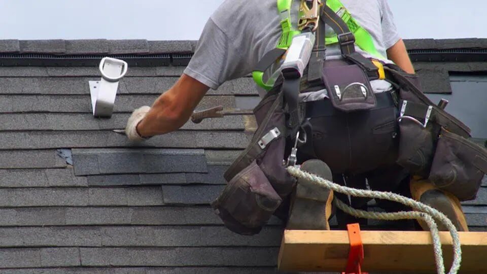 Roofer hand-nailing architectural shingles on a residential roof